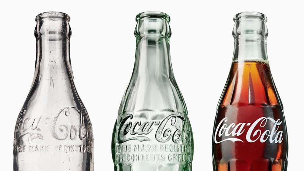 Three traditional glass Coca-Cola bottles. Two empty one full